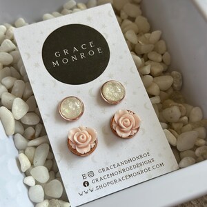 May include: A set of three pairs of earrings featuring a rose and a white iridescent design. The earrings are displayed on a white card with the text "GRACE MONROE" and social media handles for "GRACEANDMONROE" and "GRACE MONROE DESIGNS".