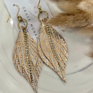 May include: Gold and white feather earrings with rhinestones. The earrings are on a white card with the text "GRACE MONROE" written on it.
