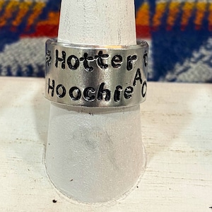 May include: A silver ring with the text "#Hotter than a Hoochie" engraved on it.