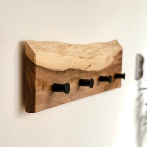 May include: A wooden wall-mounted coat rack with a natural wood finish and black metal hooks. The rack has a live edge design and is perfect for adding a rustic touch to any room.