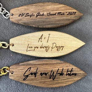 May include: Three wooden surfboard-shaped keychains with different engraved messages. The top keychain is dark brown and reads "8U Surfer Girls "Coach Nate" 2023". The middle keychain is light brown and reads "A+I Love you always Paige". The bottom keychain is dark brown and reads "Surf now. Work later."