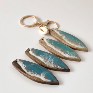 May include: Four resin and wood keychains with a blue and white ocean wave design. Each keychain has a gold ring and a small white seashell charm.