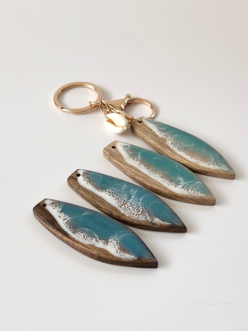 May include: Four resin and wood keychains with a blue and white ocean wave design. Each keychain has a gold ring and a small white seashell charm.
