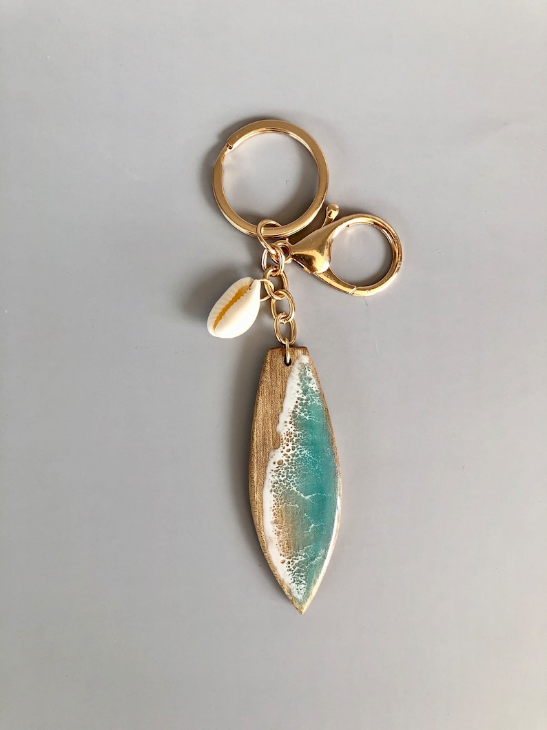 May include: Gold key chain with a surfboard charm featuring a blue and white wave design and a small white seashell charm.