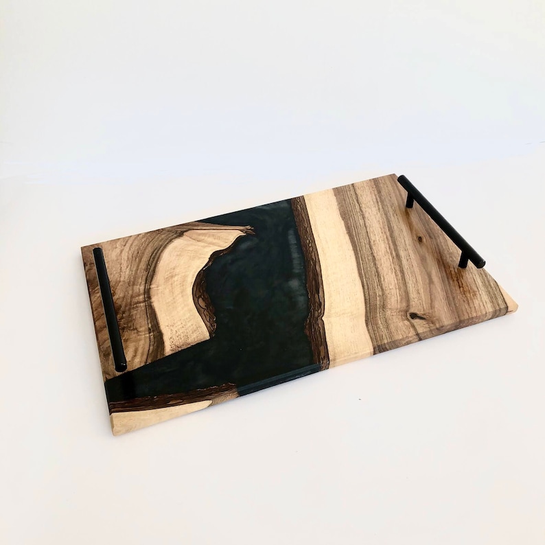 May include: A rectangular serving tray made of wood with black epoxy resin inlay. The tray has two black metal handles.