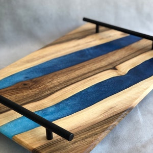 May include: A wooden serving tray with blue resin inlay and black metal handles. The tray has a natural wood finish and a modern design.