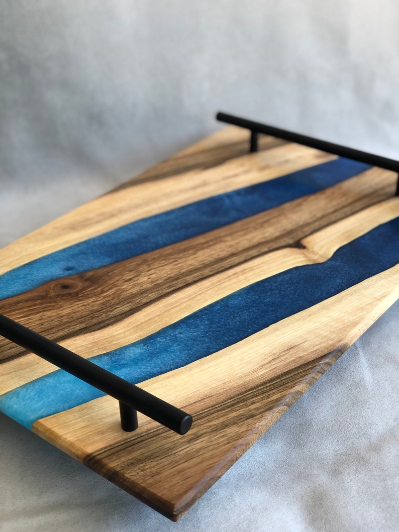May include: A wooden serving tray with blue resin inlay and black metal handles. The tray has a natural wood finish and a modern design.