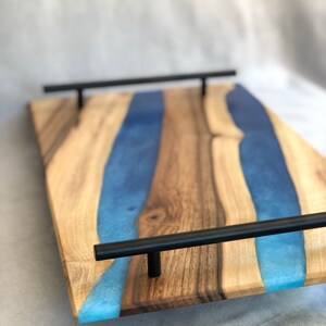 May include: A wooden serving tray with a blue resin inlay and black metal handles. The tray has a natural wood finish and a modern design.