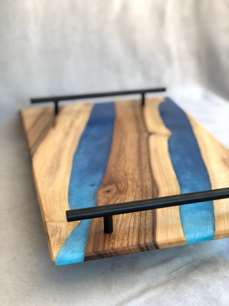 May include: A wooden serving tray with a blue resin inlay and black metal handles. The tray has a natural wood finish and a modern design.