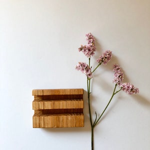 Puede incluir: Un jabonera de madera con tres compartimentos, hecha de madera marr&oacute;n claro. Una rama de flores rosas con p&eacute;talos delicados se encuentra en el lado derecho de la imagen.