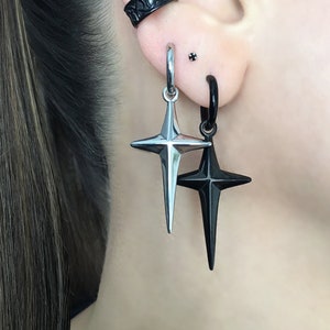 May include: A pair of earrings with a black and silver star design. The earrings are hanging from a hoop and a stud.