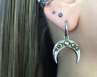 May include: Silver crescent moon earrings with gold accents. The earrings are hanging from a person's earlobe.
