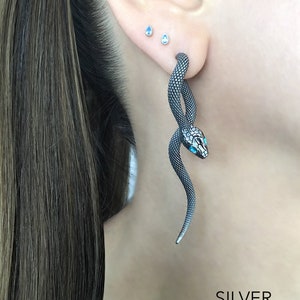 May include: Silver snake earrings with blue gemstone eyes. The earrings are a dark silver color and have a textured, scale-like appearance. The word "SILVER" is printed in white at the bottom of the image.