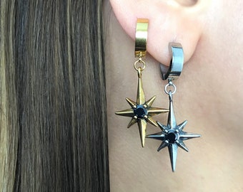 Peut inclure: Une paire de boucles d'oreilles avec un pendentif en forme d'étoile. Les boucles d'oreilles sont en métal doré et argenté et ont des pierres précieuses noires au centre des étoiles.