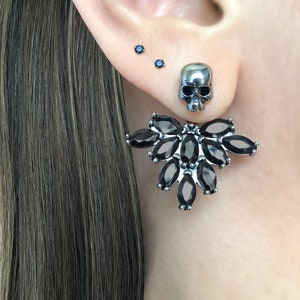 May include: A pair of silver earrings with black gemstones. One earring features a skull design, while the other has a cluster of marquise-shaped stones.