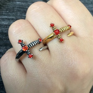 May include: Two sword rings with red gemstones. One ring is gold and the other is silver.