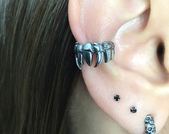May include: A silver ear cuff with a row of sharp teeth-like points. The cuff is worn on the upper part of the ear, above the lobe. The ear cuff is a popular style of jewelry for those who want a unique and edgy look.