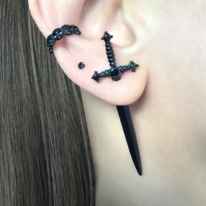May include: Black ear cuff with a skull design, a black sword stud earring with black gemstones, and a black spike earring.