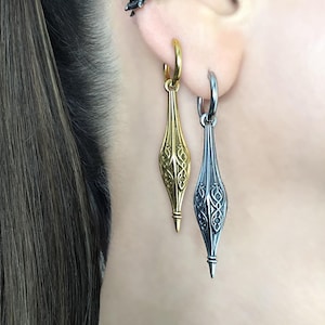 May include: Two pairs of earrings with intricate designs. One pair is gold with a pointed drop, the other is silver with a pointed drop.