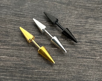 Könnte beinhalten: Drei doppelseitige Spike-Ohrringe in Gold, Silber und Schwarz. Jeder Ohrring hat einen zentralen Stab mit einem konischen Spike an jedem Ende. Die Ohrringe werden auf einer dunklen Holzmaserungsoberfläche präsentiert.