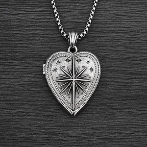 May include: A silver-toned heart-shaped locket pendant suspended from a matching box chain. The locket features an embossed North Star design at the centre, surrounded by small engraved stars and a decorative beaded border with an oxidised finish.