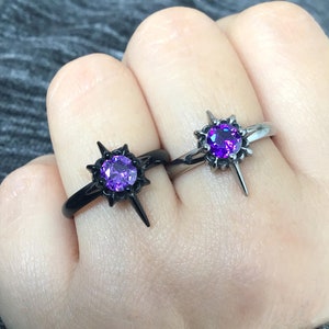 May include: Two black and silver rings with a purple gemstone in the center. The rings are shaped like a star with pointed edges.