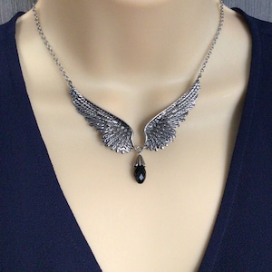 Op de afbeelding: Een zilveren ketting met een paar engelenvleugels en een zwarte kristallen hanger.