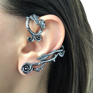 May include: A pair of silver ear cuffs with a rose and leaf design. The cuffs are worn on the upper ear and the lower ear.