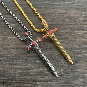 May include: Two silver and gold necklaces with sword pendants. The swords have red gemstone accents.