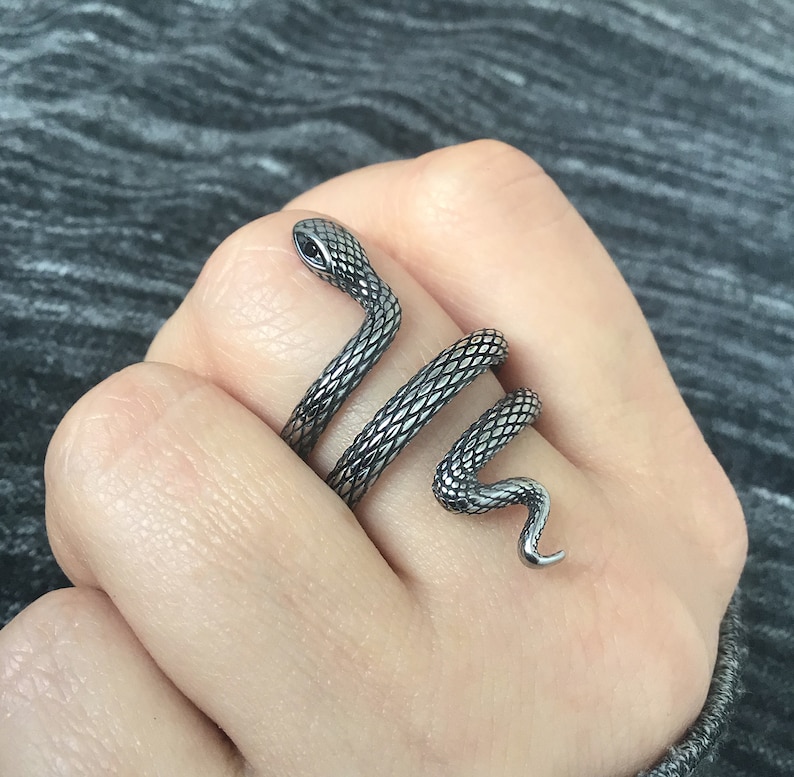 Puede incluir: Un anillo de serpiente de plata con un acabado texturizado. La serpiente est&aacute; enrollada alrededor del dedo y tiene un ojo negro.