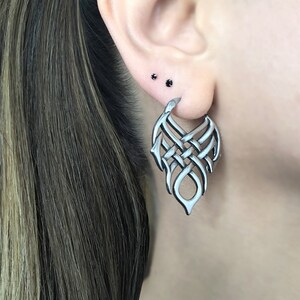 May include: Silver hoop earrings with a detailed, intricate, woven design. The earrings are shaped like a teardrop and have a dangling, open-ended design.