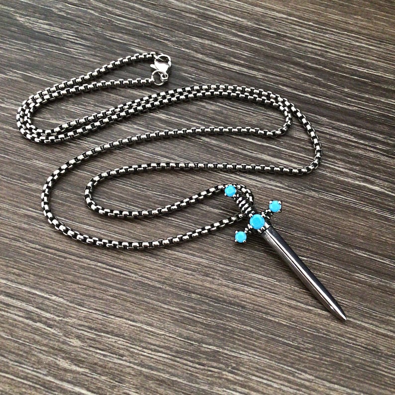 May include: A silver chain necklace with a silver sword pendant. The sword has five turquoise gemstones on the hilt.
