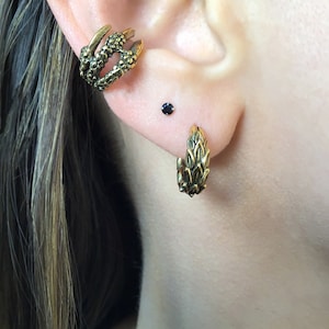 Puede incluir: Un par de pendientes de tono dorado con un dise&ntilde;o de hojas. Los pendientes se llevan en el l&oacute;bulo superior de la oreja y en el piercing helix. Un pendiente es un aro y el otro es una sola pieza.