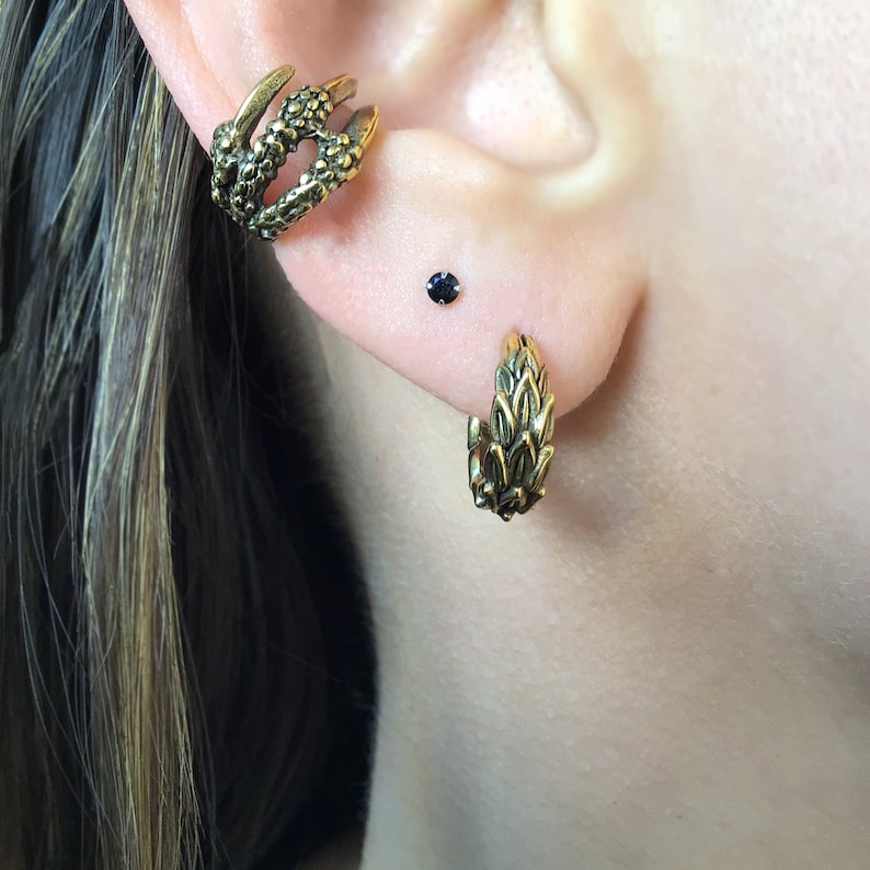 Puede incluir: Un par de pendientes de tono dorado con un dise&ntilde;o de hojas. Los pendientes se llevan en el l&oacute;bulo superior de la oreja y en el piercing helix. Un pendiente es un aro y el otro es una sola pieza.