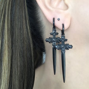 May include: A pair of black dangle earrings featuring a sword-shaped cross design with black cubic zirconia stones.