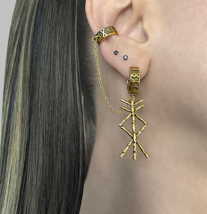 May include: Gold-toned ear cuff and earring set. The ear cuff wraps around the upper ear and connects to a hoop earring with a chain. The earring features a dangling geometric design. The jewelry has a textured finish.