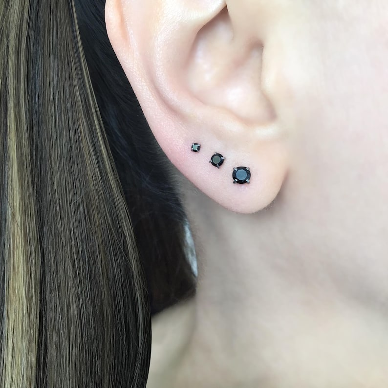 May include: Three black diamond stud earrings of different sizes. The earrings are set in silver.