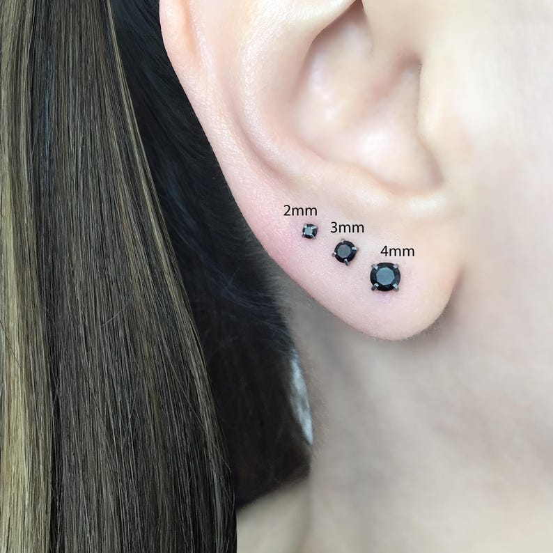 May include: Close-up of a person's ear with three black stud earrings. The earrings are labeled 2mm, 3mm, and 4mm.