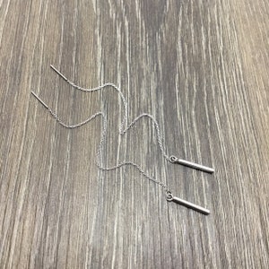 May include: A pair of silver chain earrings with a long, thin bar pendant at the end of each chain.