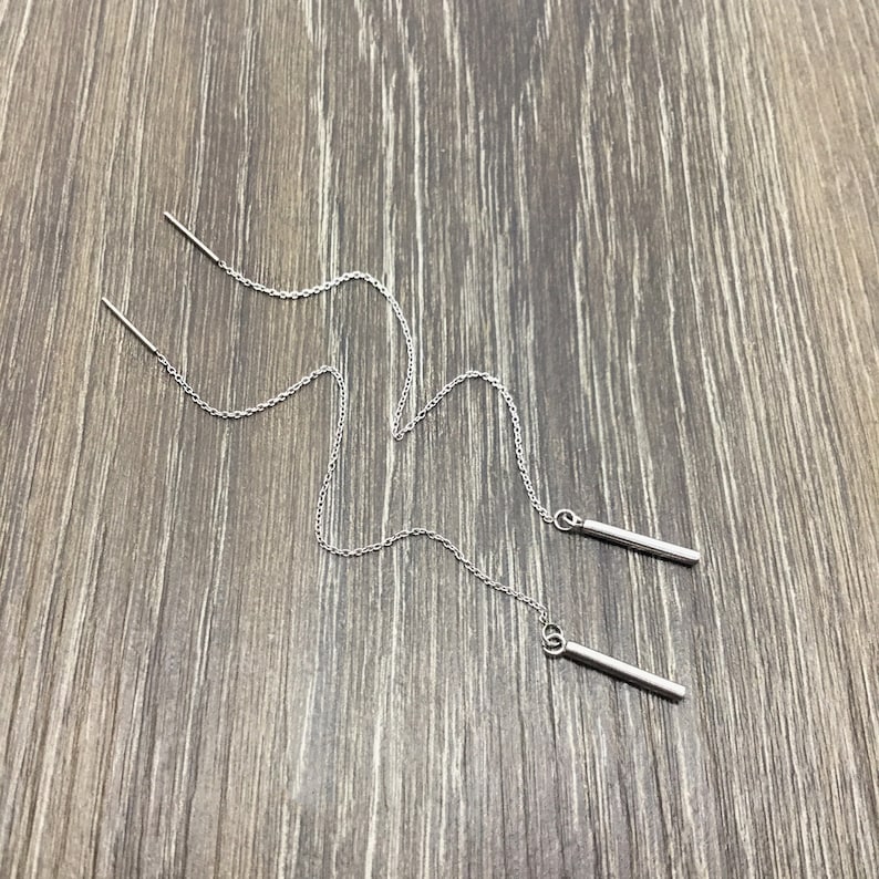 May include: A pair of silver chain earrings with a long, thin bar pendant at the end of each chain.