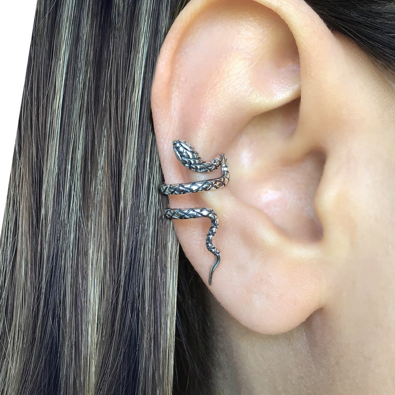 Puede incluir: Un brazalete de oreja de serpiente de plata. La serpiente est&aacute; enroscada alrededor de la oreja y tiene una superficie texturizada.