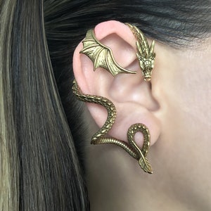 Puede incluir: Pendiente de oreja de drag&oacute;n dorado con un dise&ntilde;o detallado. Las alas del drag&oacute;n est&aacute;n extendidas y su cabeza est&aacute; mirando hacia adelante. El pendiente de oreja est&aacute; hecho de metal y est&aacute; dise&ntilde;ado para envolverse alrededor de la oreja.