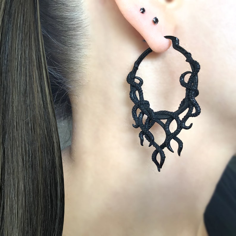 May include: Black hoop earrings with a dangling design resembling a cluster of tentacles or vines. The earrings are made of a smooth, matte black material.