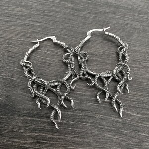 May include: A pair of silver hoop earrings with an octopus tentacle design. The earrings are large and have a detailed, intricate design.