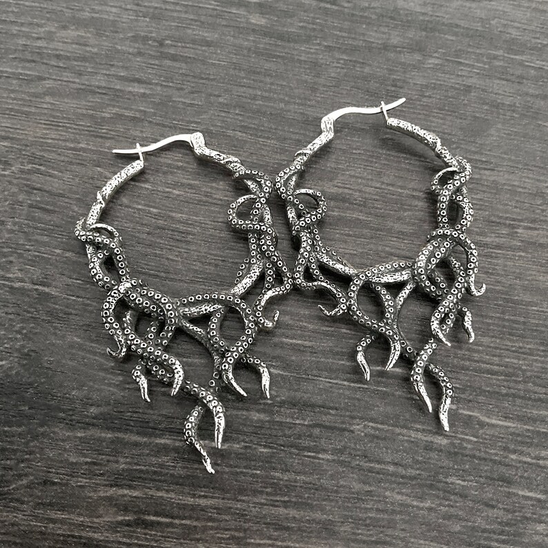 May include: A pair of silver hoop earrings with an octopus tentacle design. The earrings are large and have a detailed, intricate design.