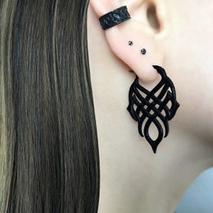 May include: Black ear cuff and dangle earrings with a geometric design. The earrings are made of a black material and have a matte finish.