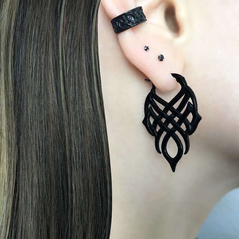 May include: Black ear cuff and dangle earrings with a geometric design. The earrings are made of a black material and have a matte finish.