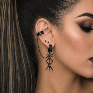 May include: Black ear cuff and earring set. The ear cuff wraps around the upper ear and connects to a hoop earring with a chain. The earring features a geometric pendant. The jewelry is black.