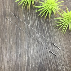 May include: A pair of silver chain earrings with a small bar pendant at the end of each chain.