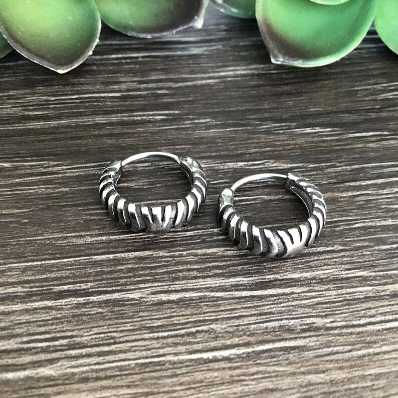 May include: Two silver hoop earrings with a textured, braided design. The earrings are on a wooden surface.